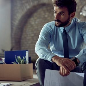 Young distraught businessman sitting in the office and thinking after getting fired from his job.